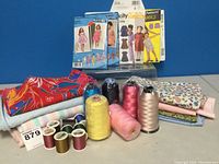Full lot showing fabrics, large and small thread spools, and girls' dress patterns arranged on blue background.