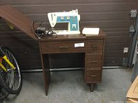 Full view of the Singer sewing machine on top of the wooden cabinet including the electrical cord and foot pedal.