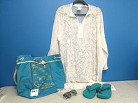 Full view of swimsuit cover, beach bag, sunglasses, and flip flops against blue background