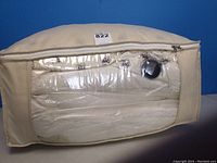 Two queen size feather beds in beige fabric vacuum seal bags with zipper and clear plastic window, placed against a blue wall.