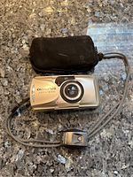 Front view of silver Olympus mju-II Zoom camera with lens extended, remote control, and black carry pouch