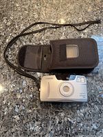 Canon Sure Shot 65 Zoom 35mm camera with carry case lying on a granite surface, camera showing front with lens and branded markings.