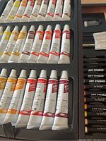 Close-up photo of multiple tubes of acrylic, oil, or watercolor paint labeled 'Art Studio' arranged in a plastic tray.