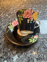 Aynsley bone china teacup and saucer with black background and colorful floral patterns arranged on a dark granite surface.