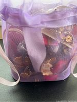 Purple sheer mesh drawstring bag containing various earrings inside, visible from front and side.