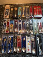 Overall view of 28 collector spoons in original boxes with various designs and origins.
