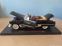 Side view of black 1949 Cadillac Coupe de Ville model with doors, hood, and trunk open on display base