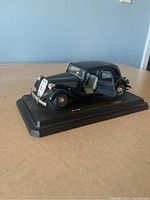 Black Burango diecast model of 1938 Citroen 15cv TA car positioned on display base with open driver side door.