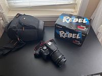 Overview of camera body with attached lens, Canon Rebel SL1 box and camera case