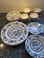 Photo showing full set of Blue Onion patterned plates, bowls, teacups, and saucers on granite counter