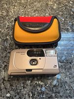 Front view of Fujifilm Fotonex 55AF camera with protective carry case next to it on granite surface.