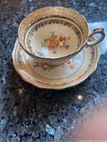 Side angled photo of the Hammersley & Co bone china teacup on the saucer showing floral pattern and gold trim