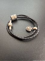 Full view of the black braided leather bracelet with two silver charms on a dark background.