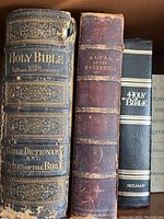 Close-up view of three religious books including a Holy Bible, Bible Dictionary and Concordances, and Altar of the Household with leather-bound and embossed spines.