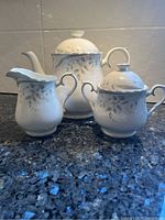 Five piece Royal Albert For All Seasons Hazy Dawn tea set showing teapot, sugar bowl, and creamer with lids on granite countertop.