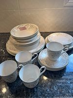 Overall view of stacked fine bone china plates, bowls, cups, and saucers with Hazy Dawn leaf pattern.