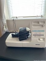 Side view showing sewing machine with programmable stitch options and foot pedal cord coiled on base.