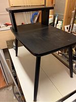 Side view of the black retro side table showing the lower and upper shelf surfaces, angled legs and matte finish.