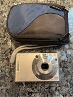 Front view of the silver Sony Cyber-shot camera with Carl Zeiss lens and case behind it