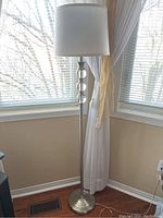Full view of the standing floor lamp with white shade and brushed metal base in corner of room.