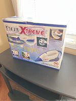 Photo showing the original box of the SteamXtreme handheld steam cleaner with product name and images.