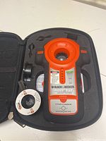 Front view of the Black & Decker Rule-Eye Stud Finder inside black molded carrying case with tape measuring wheel and manual.