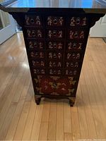 Front view showing 18 small drawers with brass ring pulls and gold tone Asian characters on red lacquered surface