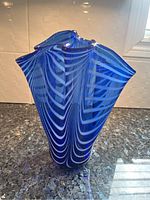 Front view of blue art deco glass vase with striped pattern and wavy top edge on granite surface.