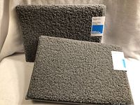 Two grey memory foam bath mats stacked, showing front texture and original product tag from Room Essentials.
