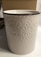 Front view of white ceramic utensil holder showing embossed geometric and floral pattern with dark edge on rim.