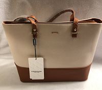 Front view of the purse showing cream top half, tan bottom half, Lovevook brand plaque and hang tag attached to one strap.