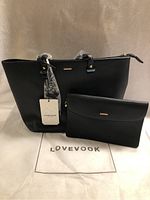 Front view of black purse and matching clutch with Lovevook tag and branded dust bag beneath