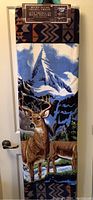 Photo of the folded throw blanket hanging, showing the deer and mountain design and geometric border pattern.