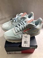 Side angle view of new Reebok running shoes with tags attached, resting on shoebox showing brand and model details.