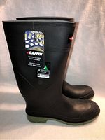 Side view of black rubber boots with tags showing brand and manufacturing details.