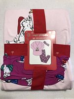 Folded new pajama set with tags showing pink top and purple pants with cat prints wrapped with red ribbons and label showing size 1X