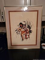 Framed picture of a warrior in a dynamic pose holding a circular object with a buffalo design, visible signature at lower right.