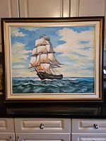 Frontal view of the framed original sailboat painting showing the full artwork including sky, water, and ship with sails.