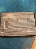 Front side of rectangular silver cigarette case showing engraved initials and etched line pattern
