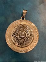 Front view of the large circular Aztec calendar pendant showing detailed sun face and calendar design with textured border.