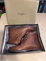 Pair of new Goodfellow & Co men's brown leather boots shown inside open shoebox with original packaging visible.