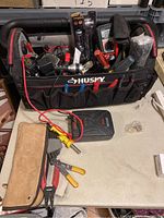 Husky branded soft-sided toolbox full of assorted tools including electrical clamps, pliers, and a battery charger.