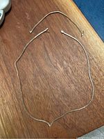 Image of a long silver chain necklace and a silver chain bracelet side by side on a wood surface.