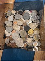 Top-down view of a box filled with mixed foreign coins of different sizes and metals showing a wide variety of designs and wear levels.