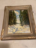 Framed oil painting front view showing winter landscape with pine trees and snow.