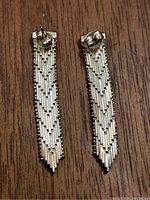 Pair of silver earrings with textured geometric pattern, laid flat on wooden surface.