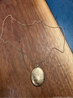 Full view of the antique oval locket pendant with attached chain laid on wooden surface.