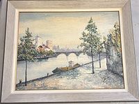 Framed oil painting showing a riverside scene with arborous trees, buildings, and an arched bridge in the distance. Signed at lower right 'Darwin'.