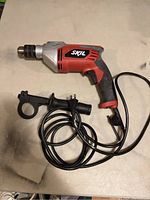 Full view of Skil hammer drill with side handle and cord on surface.