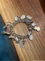 Photo showing front side of vintage silver charm bracelet with assorted charms including red flower, cat, gavel, and buildings.
